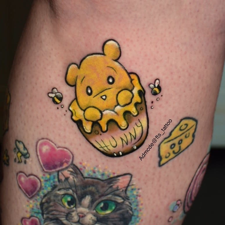 Cute tattoo of a mini Winnie the Pooh peeking out of a honey pot labeled 'Hunny,' with bees buzzing around